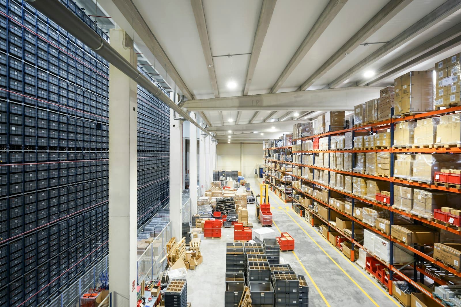 Interior of a large industrial warehouse — wide aisle with high-bay racking and stored pallets under overhead lighting.