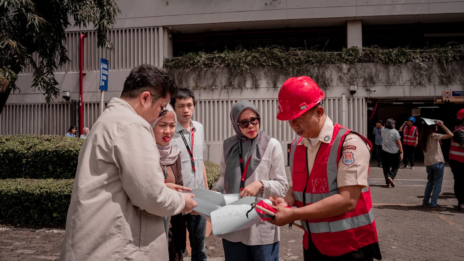 A project team reviewing plans on a commercial jobsite while a supervisor in a red hard hat and hi-vis vest points at the drawings.